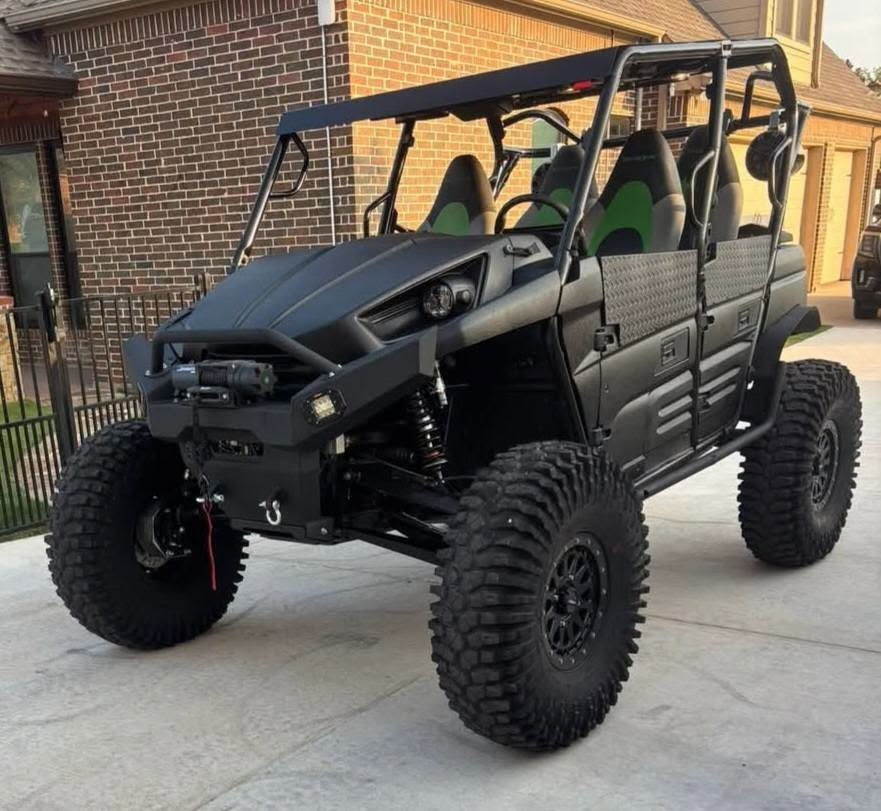 Customized Kawasaki Teryx 4 with upgraded suspension, larger off-road tires, front winch, and accessories parked after receiving a custom Bandit Black Label suspension setup.