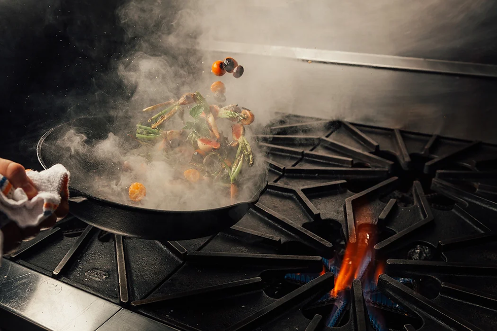 A pan in which vegetables are being tossed letting out a lot of smoke