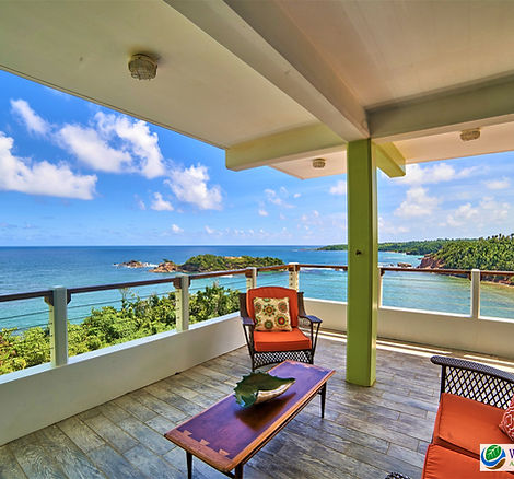 Oceanfront balcony at Wanderlust Caribbean boutique hotel in Dominica, featuring a cozy seating, and panoramic views of Hodges Bay and lush coastal landscapes.
