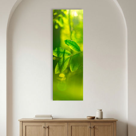 Metallic glass print hanging on the wall, featuring luminous green leaves in soft golden forest light