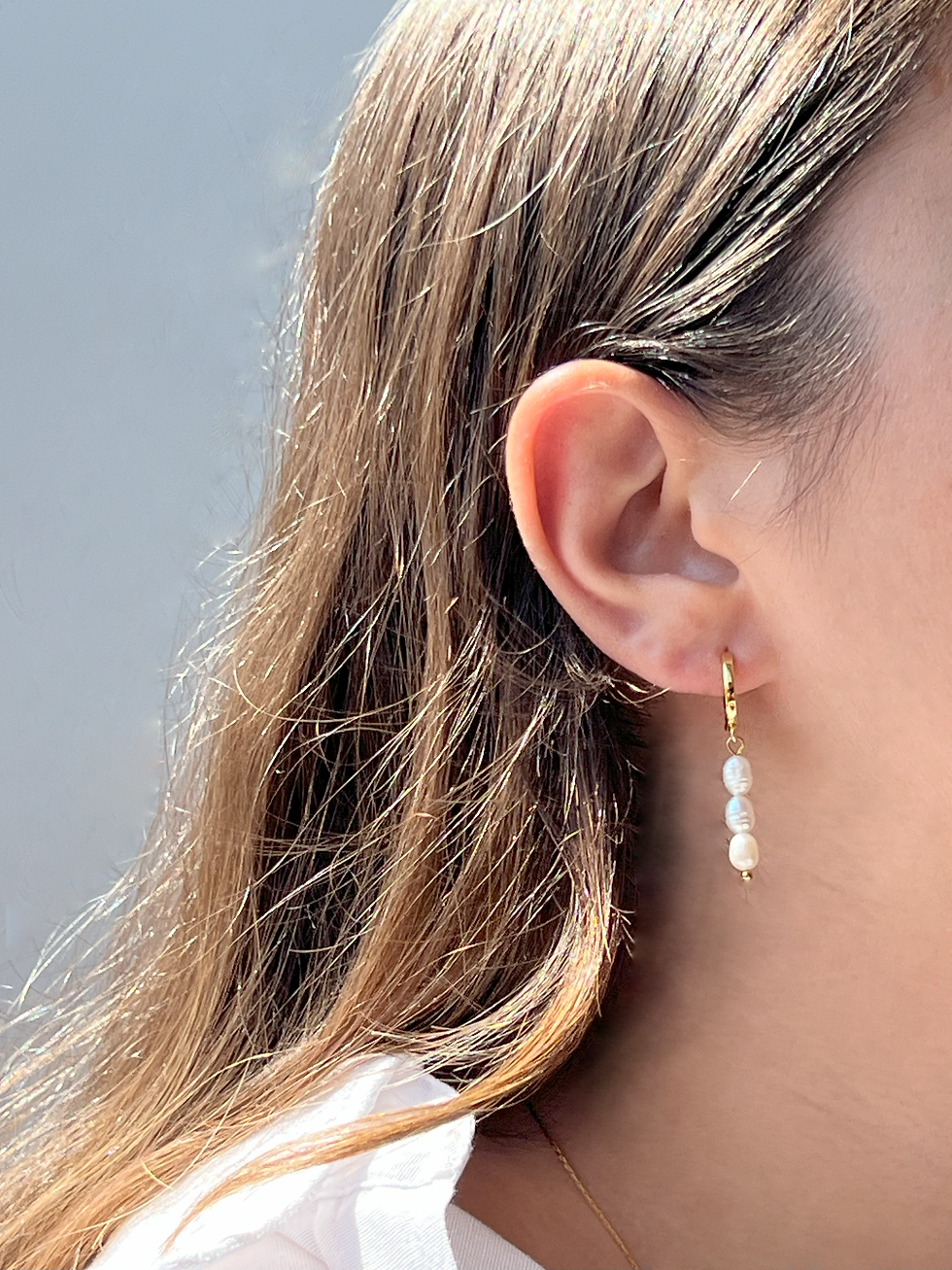 אדם עונד עגילים תלויים מציפוי זהב עם פנינים לבנות, Pearl Kiss.