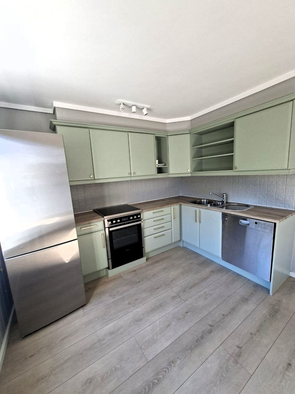 Modern kitchen with green cabinets and stainless steel appliances.