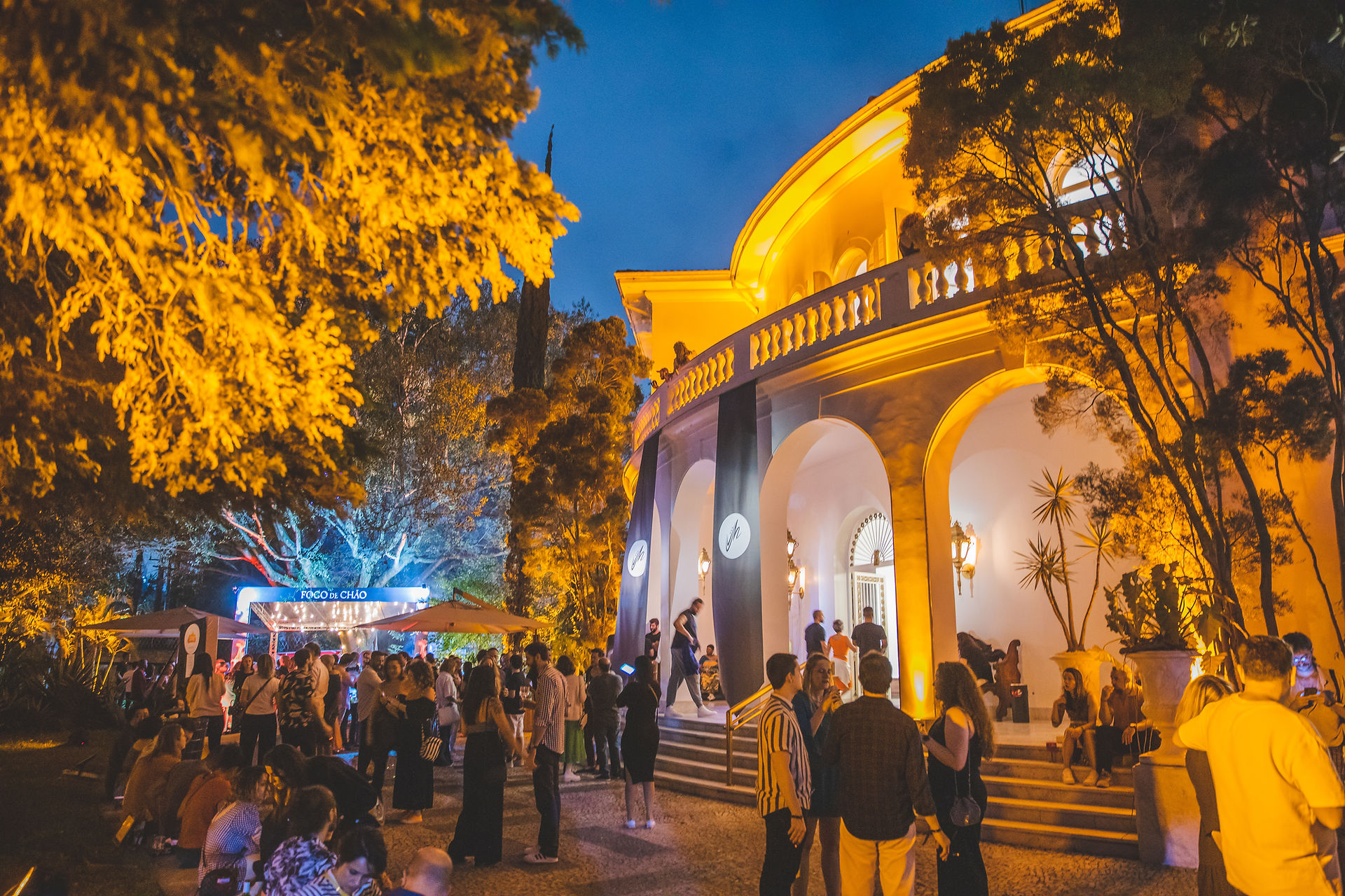 Fachada principal do Nacional Club iluminada durante a noite, com visitantes circulando pelos jardins e pela entrada do festival. A imagem destaca a atmosfera acolhedora e a ocupação do espaço histórico pela Jazz Mansion.