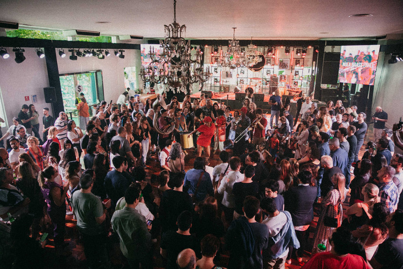 Banda de metais se apresenta cercada pelo público em um dos salões da Jazz Mansion. A imagem evidencia a proximidade entre artistas e espectadores, característica da experiência imersiva do festival.