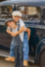 photo de deux frères enfants avec des bérets, une salopette et une voiture vintage en arrière plan.