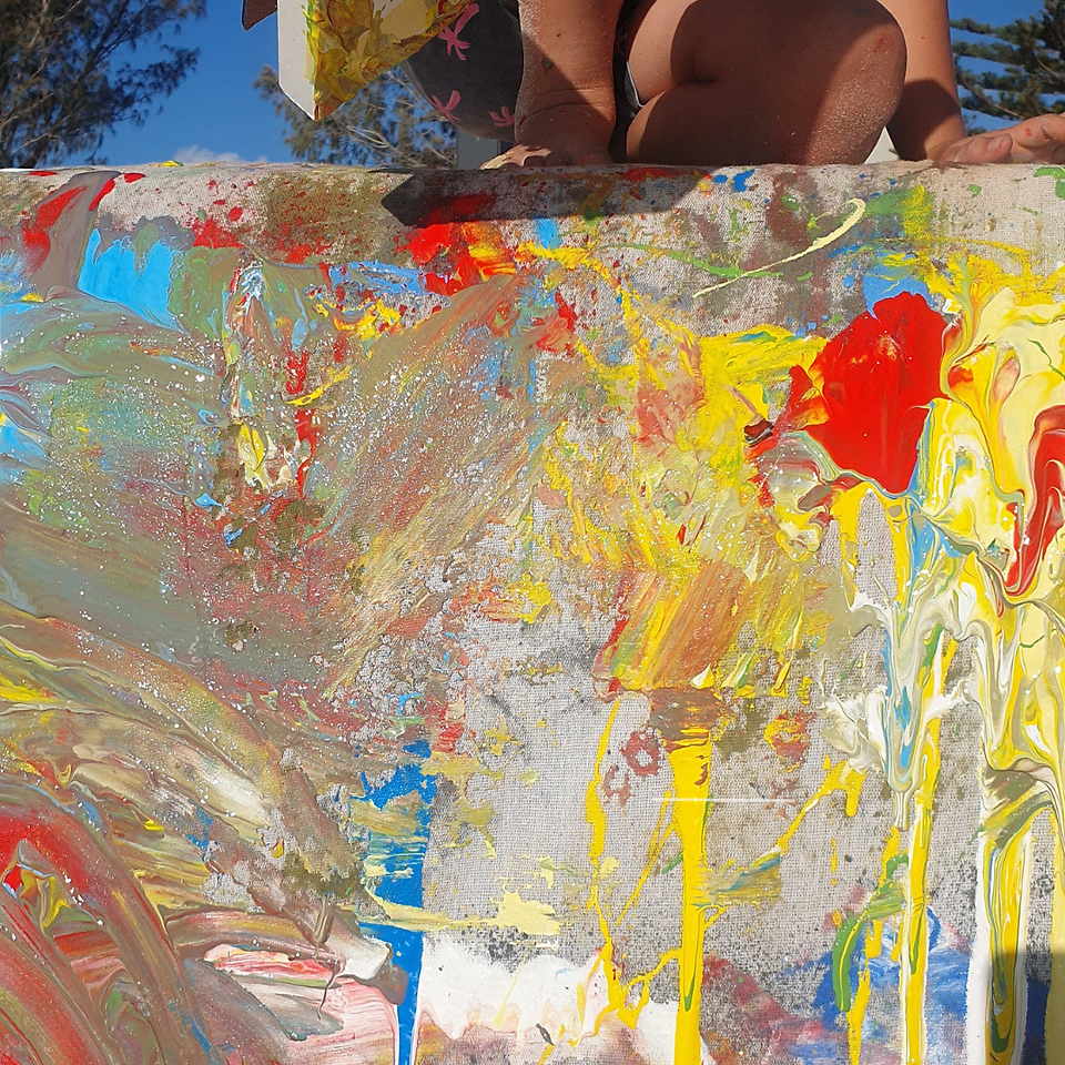 Child kneels down to paint on the paint waterfall which is a large canvas over a wall