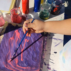 child's hand painting a canvas with purple and pink paint