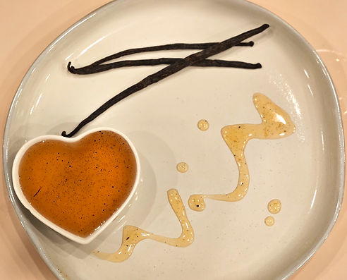 Vanilla syrup in a heart-shaped dish on a white plate with drizzled syrup and vanilla bean pods.