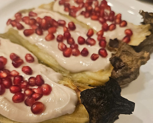 Vegan roasted eggplant topped with creamy tahini sauce and fresh pomegranate seeds