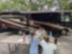 Family eating at a picnic table outside a black-and-cream Sunstar RV, with children and an adult sharing a casual meal outdoors