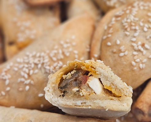 Golden vegetable-stuffed burekitas sprinkled with sesame seeds, with one cut open showing savory filling.