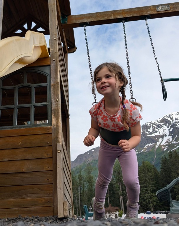 Child swinging in a playground, with mountains in the horizon