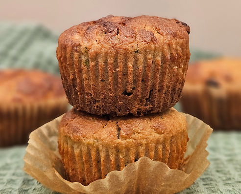Vegan zucchini raisin muffins stacked on a green cloth, with a golden brown crust and soft texture.