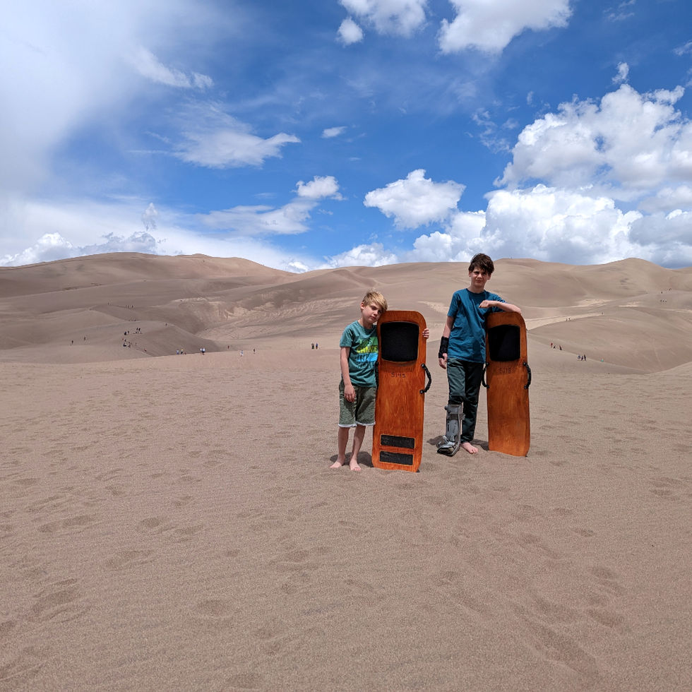 2 kids holding sleds on sand dunes, on a sunny day with partly cloudy skies