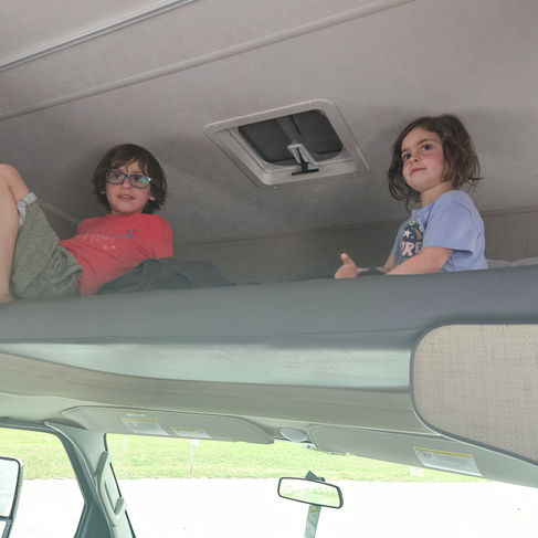 2 kids sitting above the cab on a bed in an RV