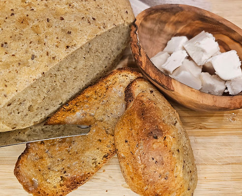Homemade kids-approved white bread loaf with slices on a cutting board, served with a wooden bowl of vegan butter cubes.