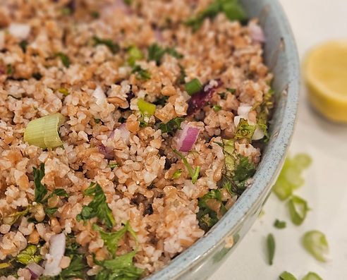 Bowl of bulgur salad mixed with herbs, green onions, and red onion.