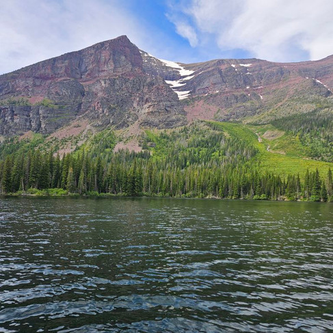 lake water surrounded by trees and snow-peaked mountains in a partly-cloudy day