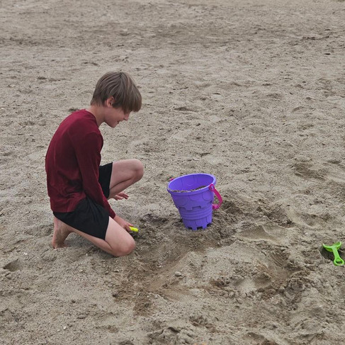 a boy sitting on a sandy beach, playing with beach toys