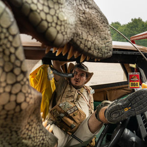 A park ranger looks frightened as a animatronic dinosaur open its mouth looking as if it's going to eat the ranger