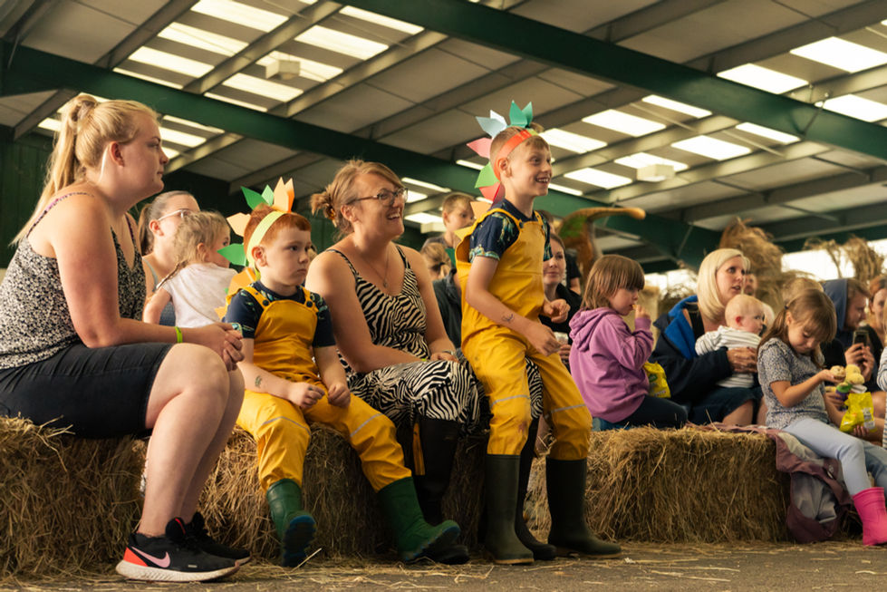 Family watches on sat on hay bales with dino hats on