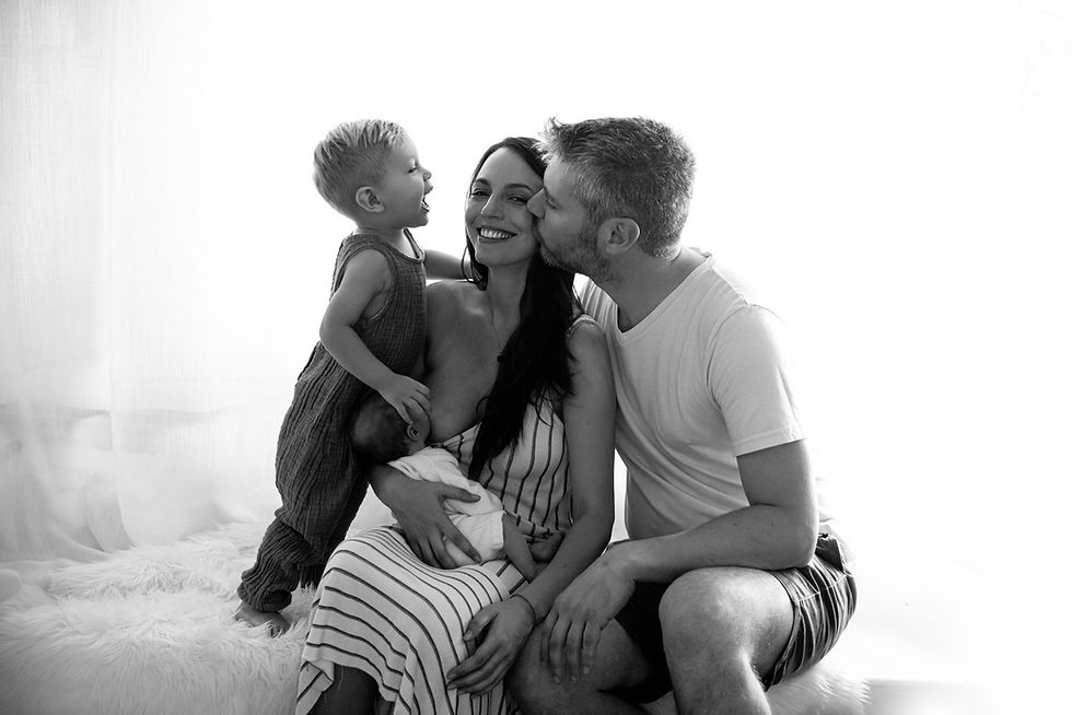 Mamá amamantando a su bebé recién nacido mientras papá y su hijo la besan durante una sesión de fotos newborn a domicilio en Punta del Este – Onedrop Photography