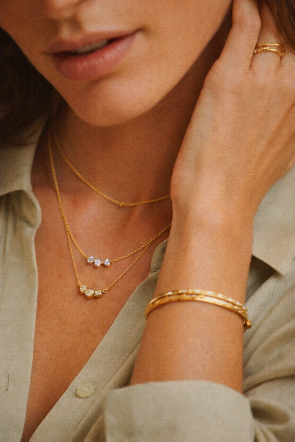Plano detalle del cuello y la mano de una mujer que lleva tres collares, una pulsera y un anillo dorados