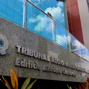 Fachada do Tribunal Regional Eleitoral de Pernambuco, Edifício Antônio Camarotti. Vidros refletem céu azul. Plantas e brasão visíveis.