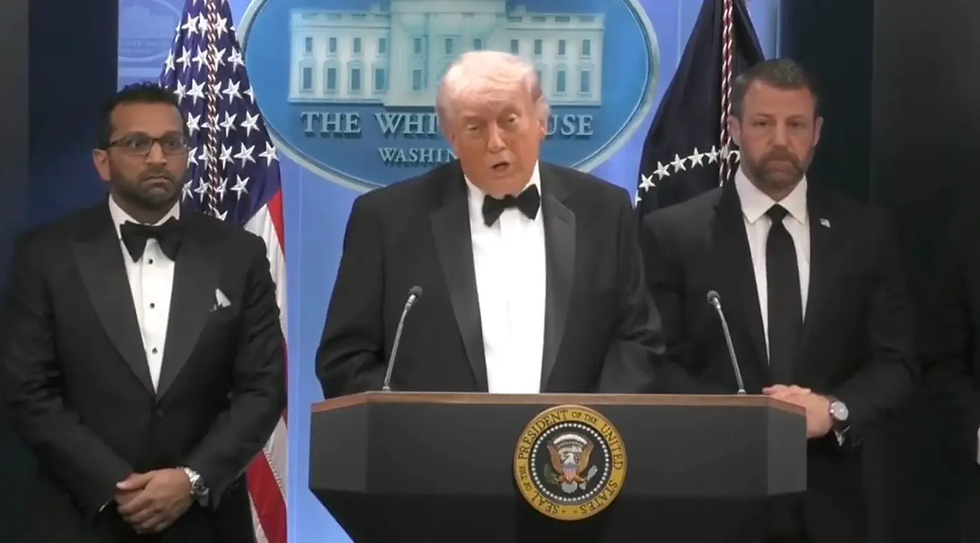Três homens de terno preto em um pódio com o selo presidencial. Fundo azul com bandeiras americanas e logotipo da Casa Branca.