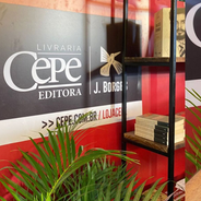 Estande da Livraria Cepe Editora com livros em prateleiras, plantas verdes e painel vermelho-preto com texto J. Borges.