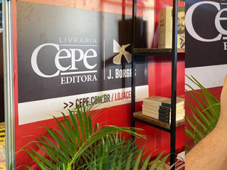 Estande da Livraria Cepe Editora com livros em prateleiras, plantas verdes e painel vermelho-preto com texto J. Borges.