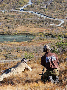 Two snipers on a hill, one aiming a rifle, the other observing