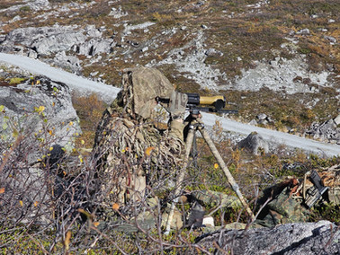 Camouflaged sniper with rifle on tripod in autumn terrain
