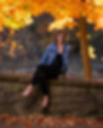 Image of Christie Green, solo entrepreneur and founder of ChristieLiz Consulting, seated on a stone wall with autumn leaves and orange trees behind her and at her feet.