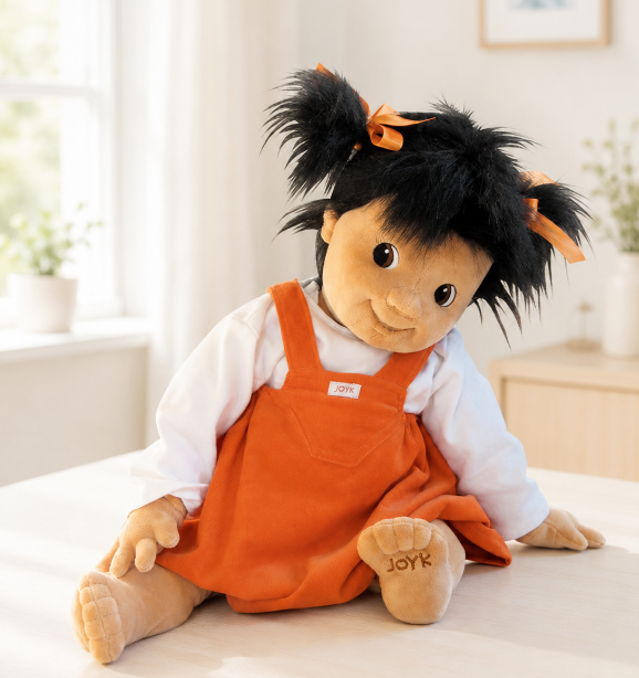 Demenzpuppe Emilie in einem orangen Kleidchen und mit schwarzen Haaren