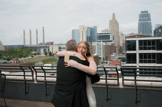 A bride and her dad hug after a first look on Corrigan Station rooftop overlooking downtown kansas city