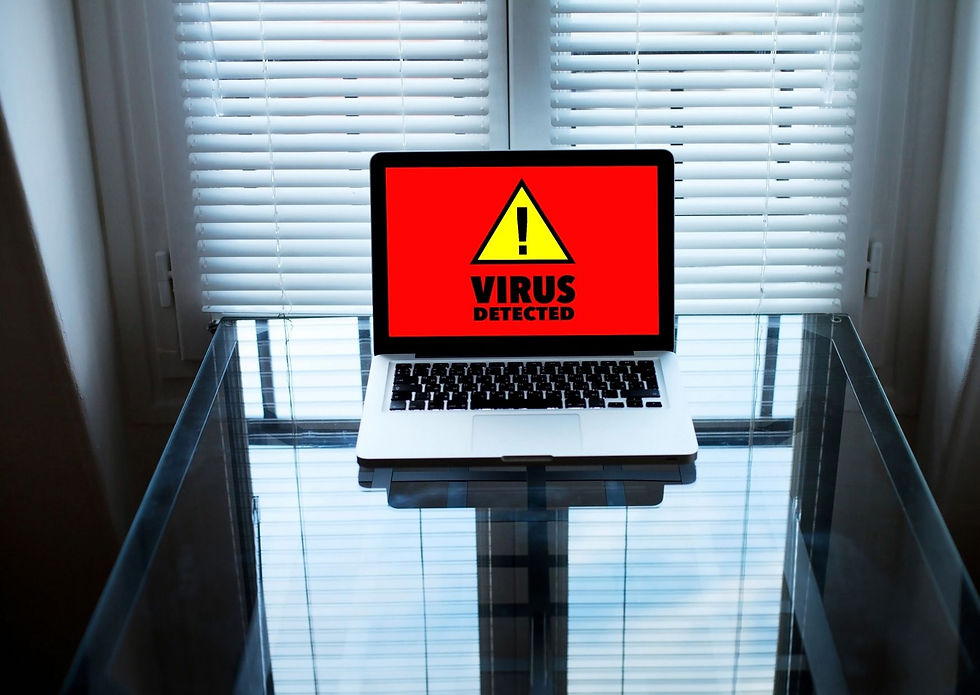 Laptop on glass table with a "Virus Detected" warning on screen. Red background, yellow triangle alert. Window blinds in the background.