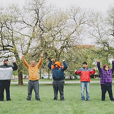 Diverse male and female participants in the LSE program with their arms up in the air together in Humboldt Park. 