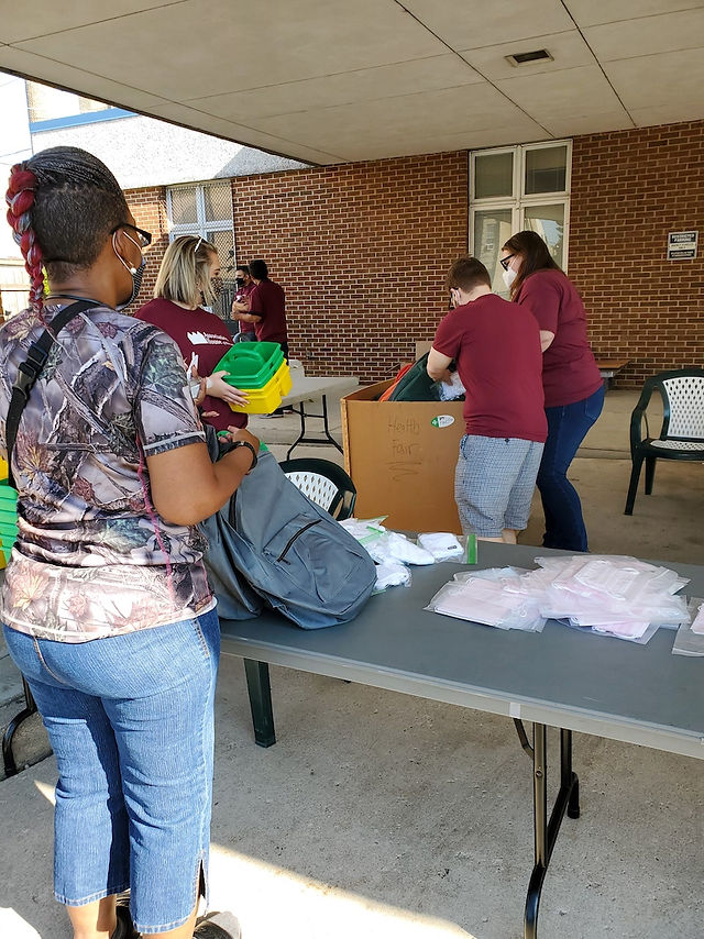 A black mother grabbing school supplies from volunteers. 