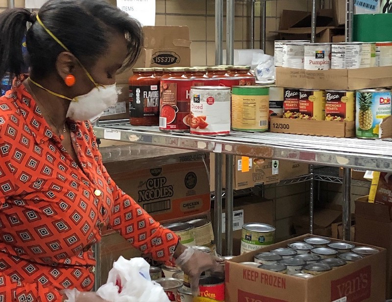 A black female food pantry worker stocking the shelves with goods.