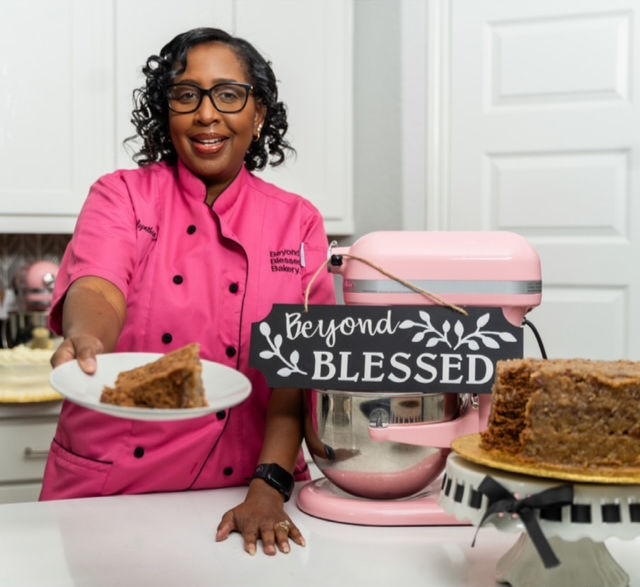 Smiling baker with slice, pink mixer, and baked cake