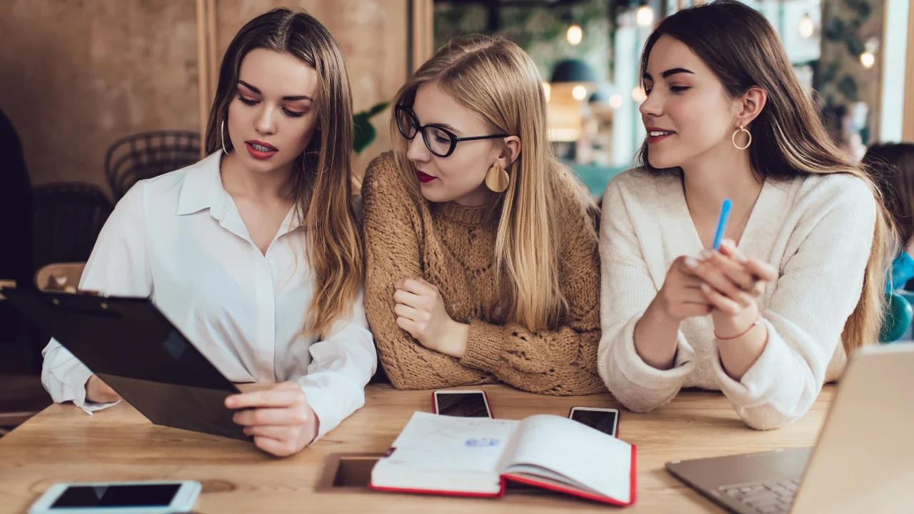 3 chicas sentadas en una mesa miran atentas una tablet