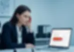 Mujer de traje observa con expresión seria la pantalla de su laptop que muestra una reseña en Google Business Profile con calificación de cinco estrellas. La escena sugiere análisis de reputación en línea o gestión de comentarios digitales.