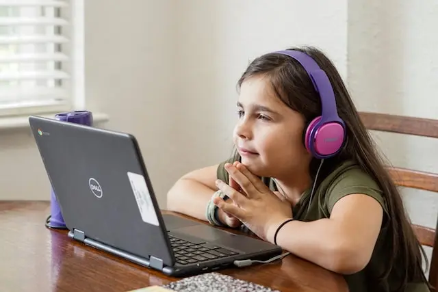 Niña con audífonos frente a una laptop