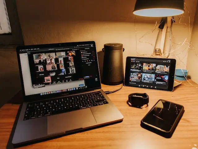 Laptop y tablet sobre mesa de madera mostrando ambas una videoconferencia