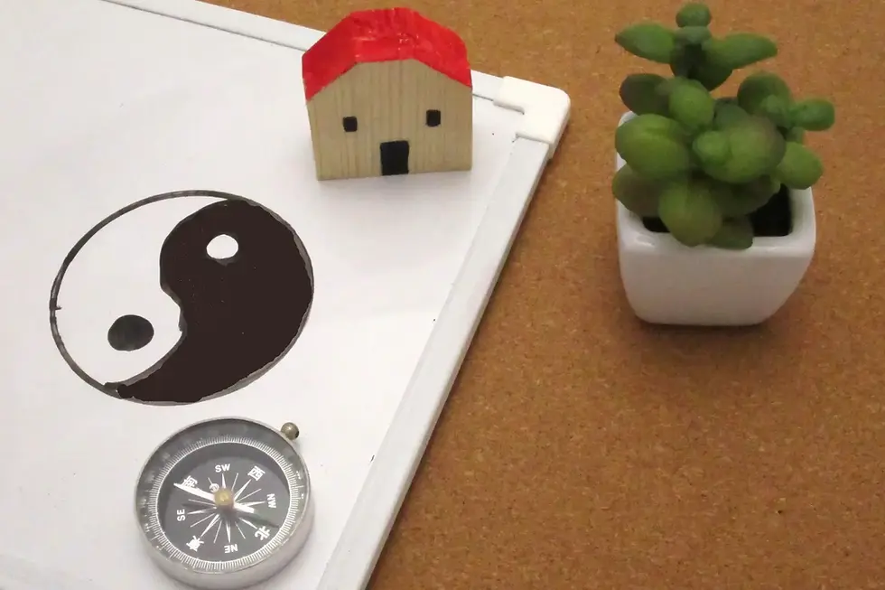 Pizarra blanca con Yin Yang dibujado, brújula, casita de cartón y planta pequeña