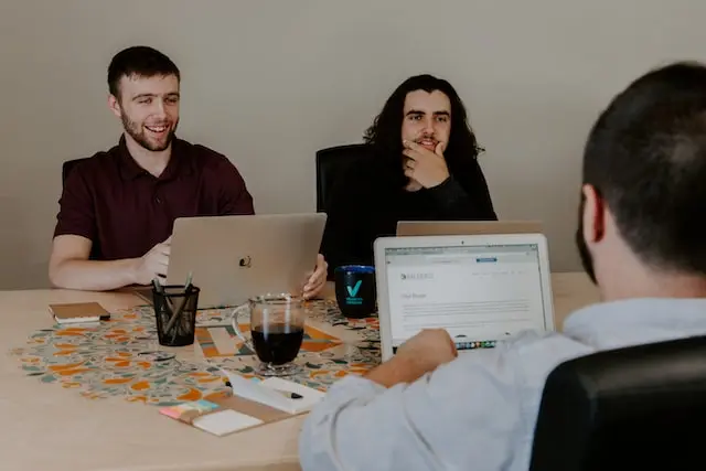 Jóvenes platicando sentados en una mesa frente a sus laptops