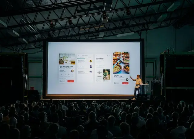 Hombre señalando una pantalla mientras imparte una conferencia