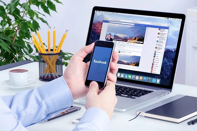 Persona viendo Facebook en un smartphone y un ordenador