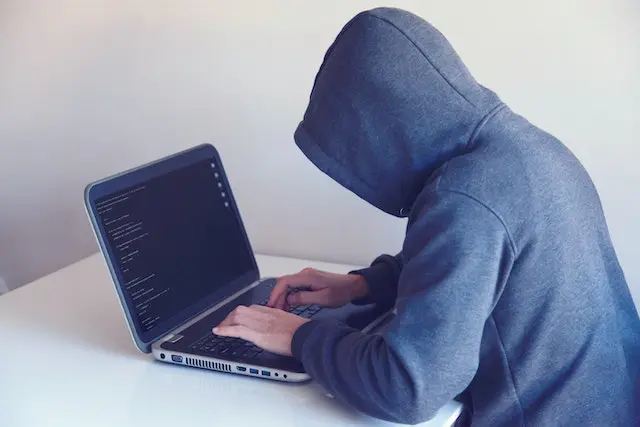 Persona misteriosa, vestida con hoodie gris, escribe en una laptop